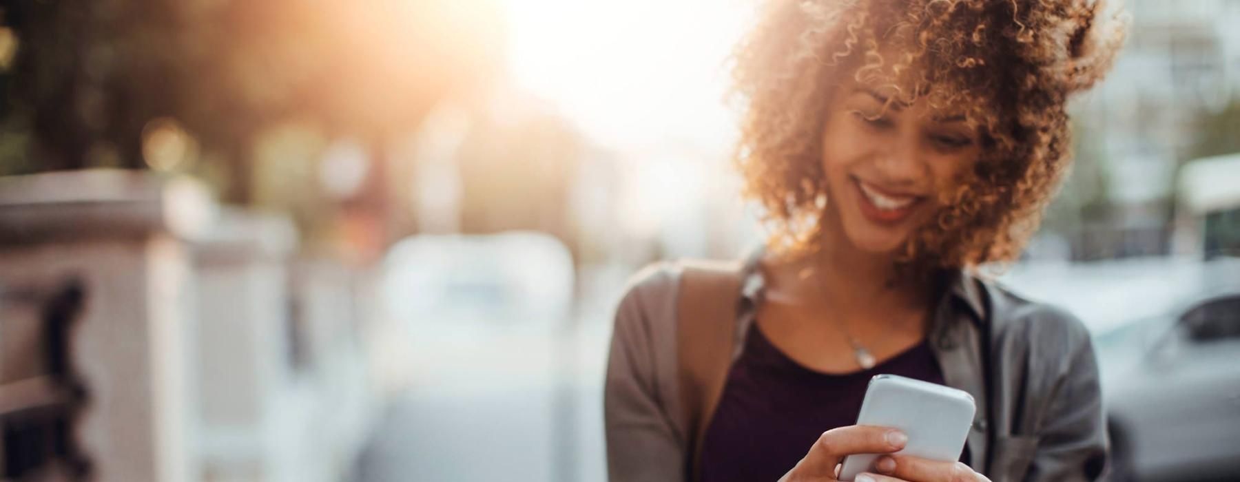 woman texts on her phone as she walks through the city