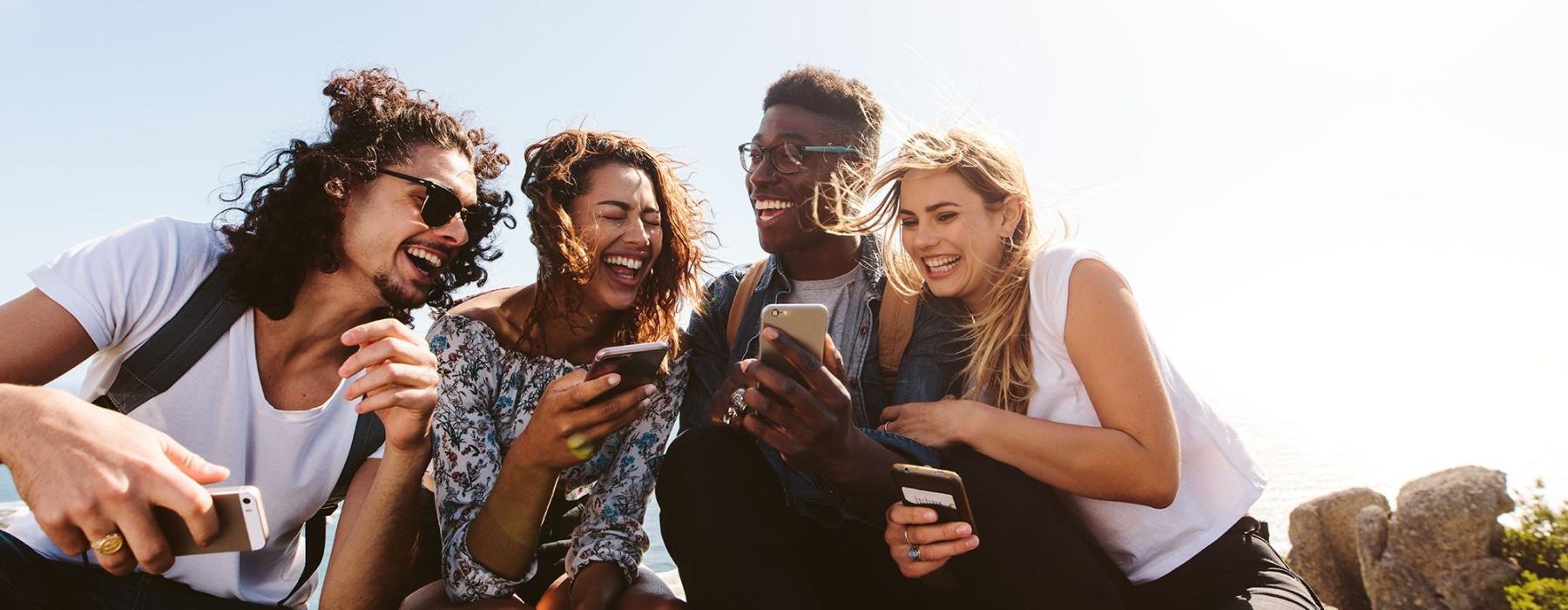 a group of friends sit outside laughing over their cell phones